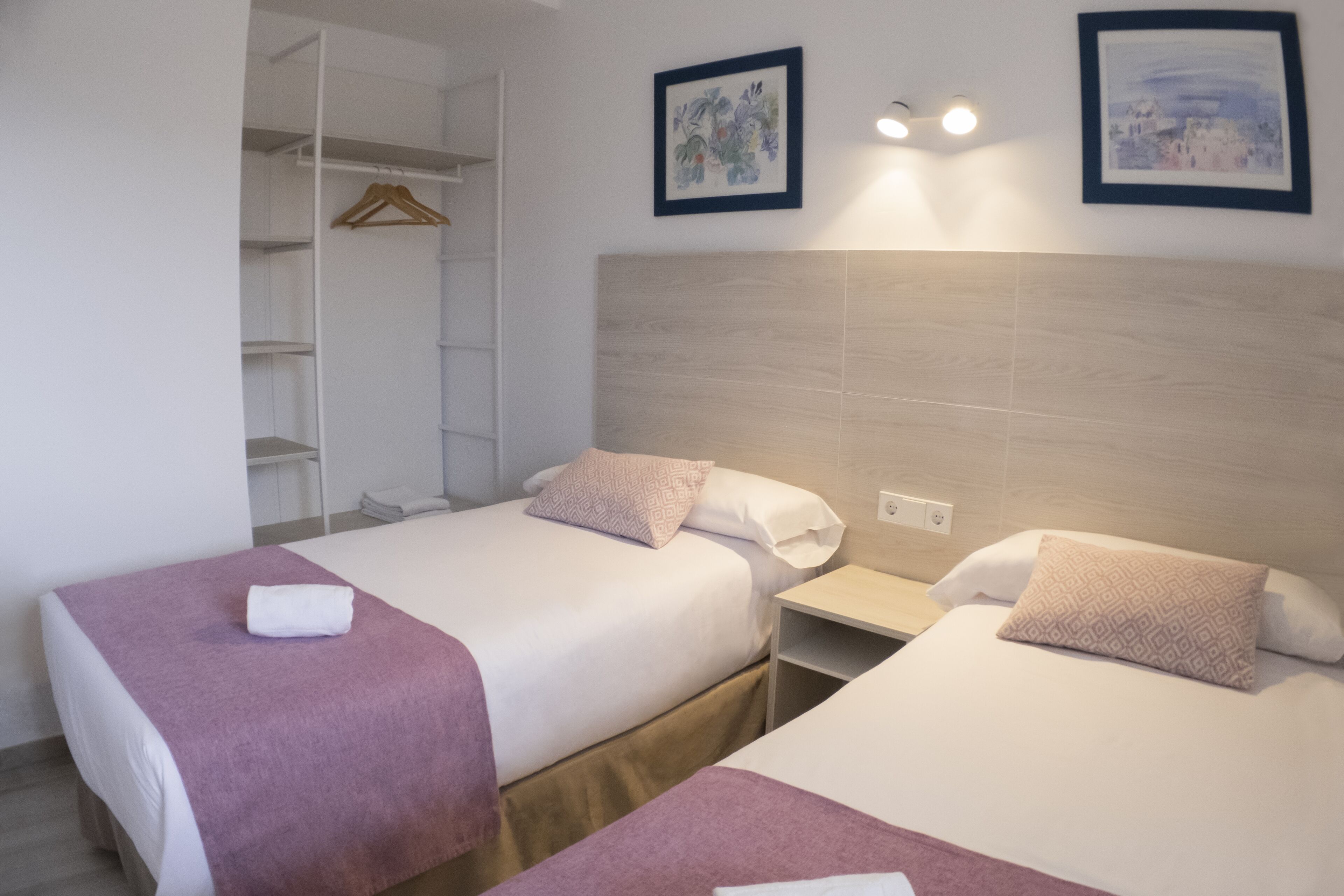 A hotel room with two beds, a wardrobe, and a nightstand.