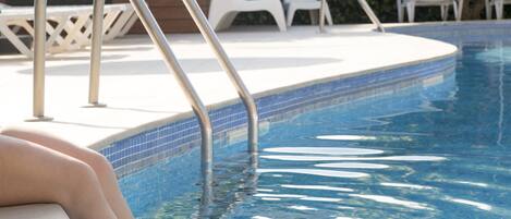 Una piscina con escaleras metálicas y sillones blancos al fondo.
