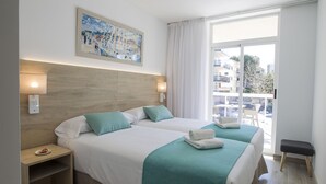 A hotel room with two beds, a wooden headboard, a painting, a balcony with a view of buildings, and a bench. - Aparthotel CYE Holiday Centre (Salou)