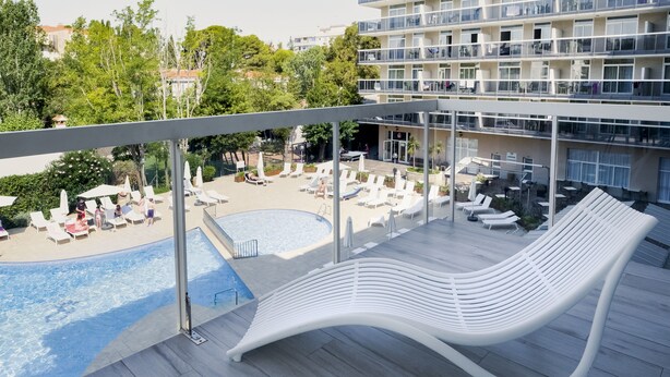 A modern hotel balcony with a pool, lounge chairs, and a unique white bench. - Aparthotel CYE Holiday Centre (Salou)