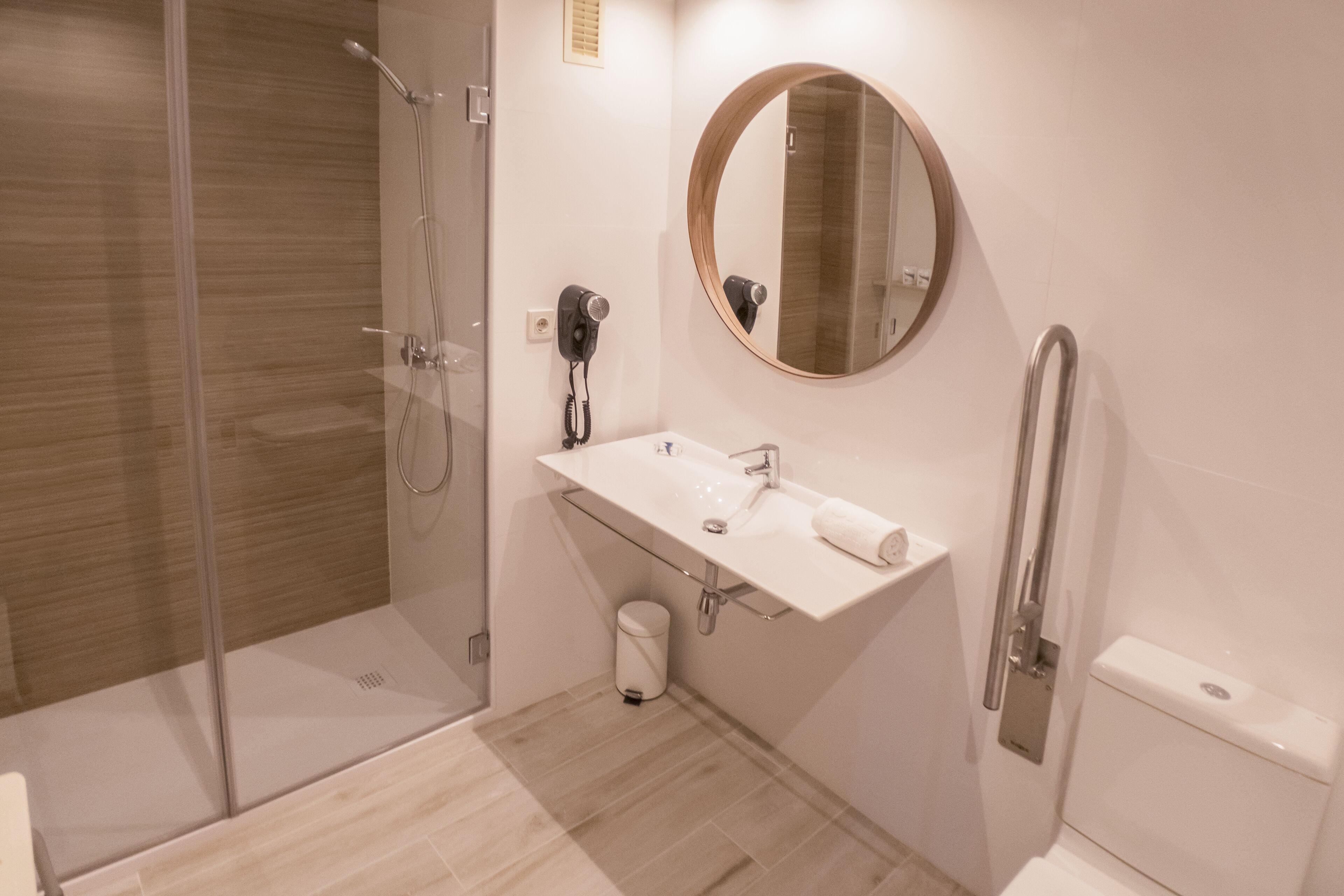 A modern bathroom with a glass shower enclosure, a white sink with a mirror above it, and a toilet.