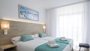 A hotel room with two beds, a wooden headboard, a painting on the wall, and a bench by the window. - Aparthotel CYE Holiday Centre (Salou)