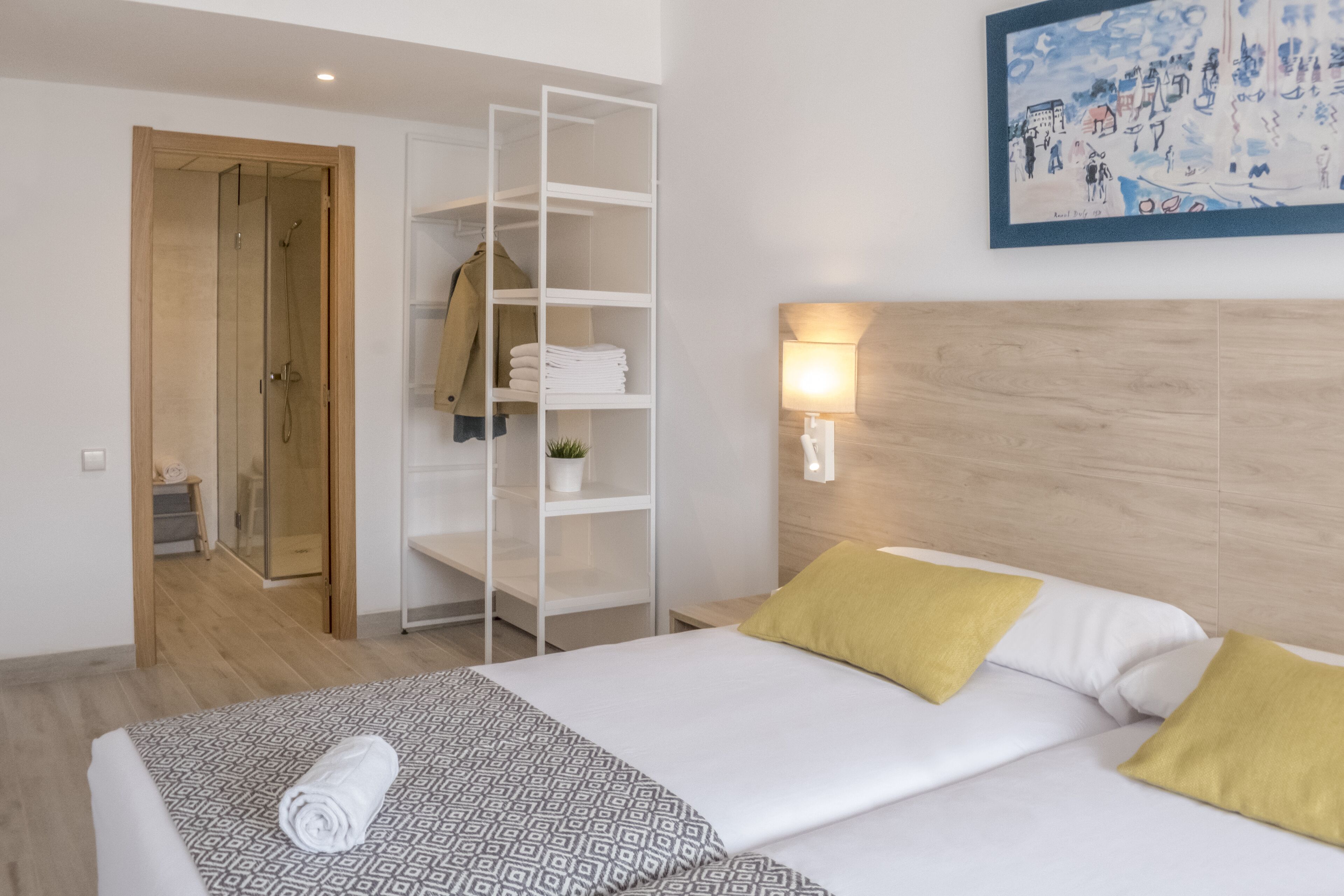 Una habitación de hotel con cama, armario, estantería, un cuadro y una lámpara de pared.