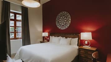 A hotel room with a large bed, two bedside tables with lamps, a wooden headboard, a decorative wall piece, and a window with curtains.