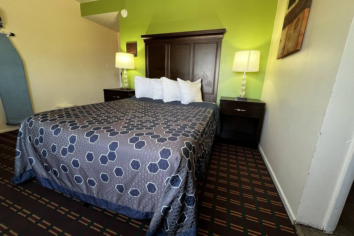 A hotel room with a large bed, two bedside tables with lamps, a green accent wall, and a patterned carpet.