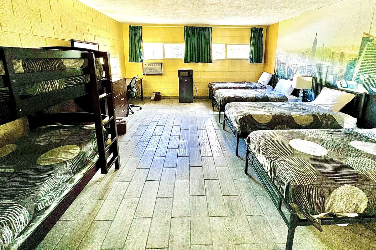 A dormitory room with bunk beds, a tiled floor, and a cityscape mural on the wall.