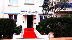 A hotel entrance with a red carpet leading to the door, surrounded by greenery. - Hôtel Le Petit Château (Cannes)