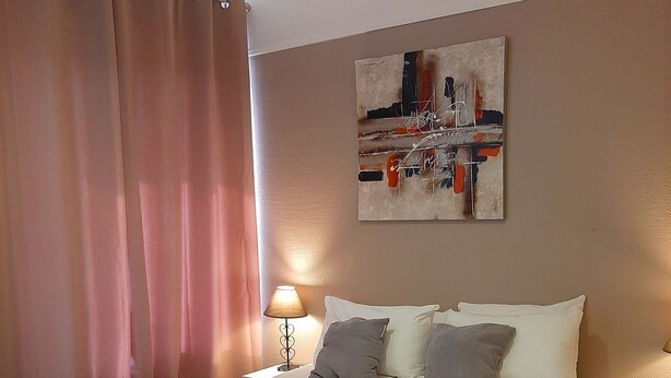 A neatly made bed with a black throw, a bedside lamp, and a wall art piece above it. - Hôtel Le Petit Château (Cannes)