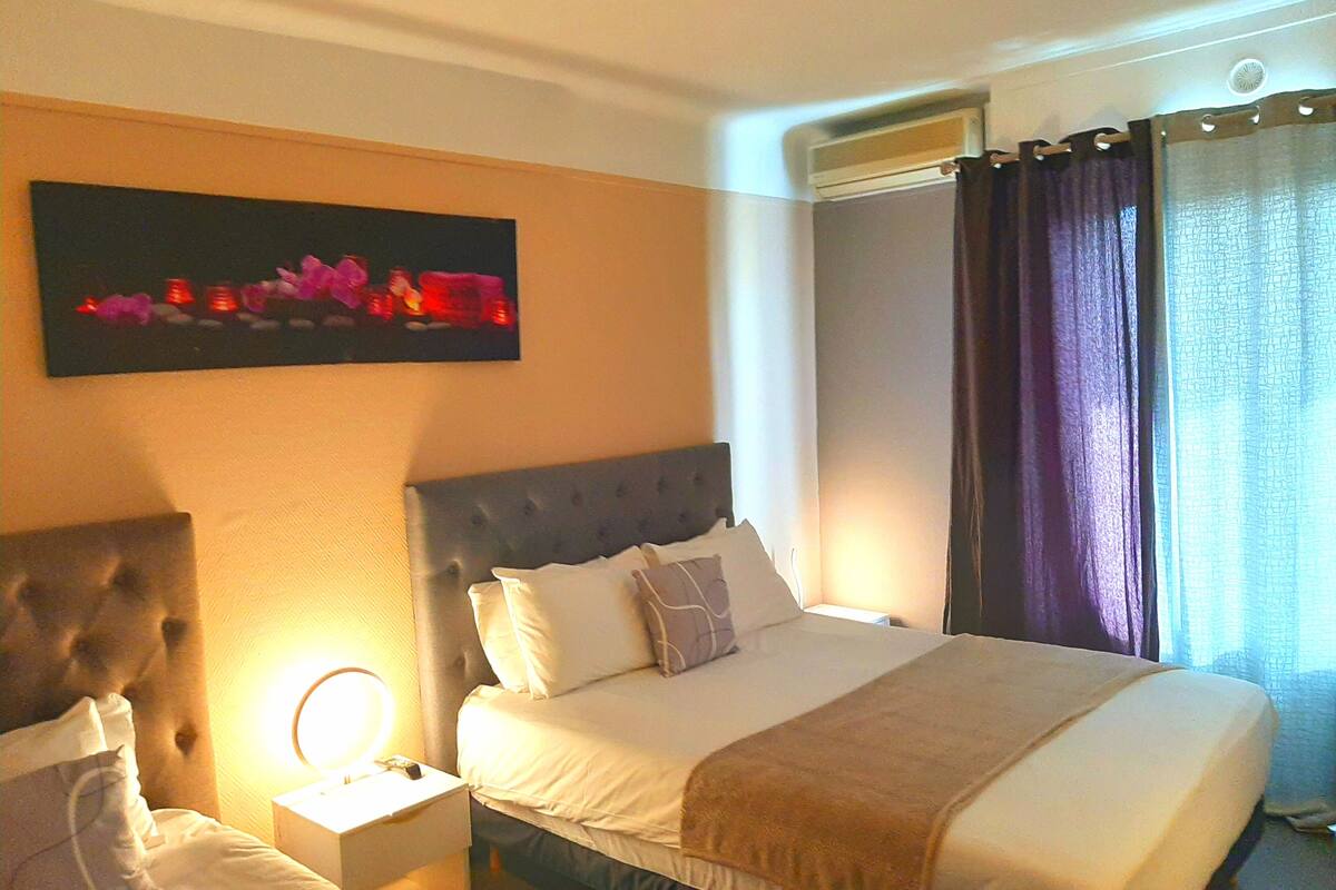 A hotel room with a large bed, a nightstand with a lamp, a headboard, and a painting on the wall.