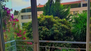 A balcony with a chair and table, overlooking a garden with various plants and a building in the background. - Hôtel Le Petit Château (Cannes)