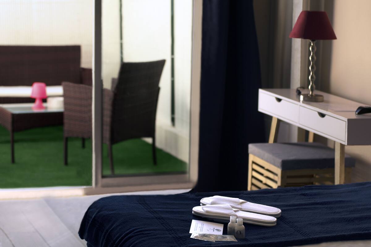 A hotel room with a bed, a desk, a chair, a lamp, and a view of an outdoor area with a chair and a table.