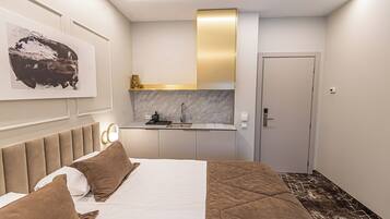 Una habitación de hotel moderna con una cama, una mesita de noche, un espejo, un cuadro, una kitchenette y una puerta.