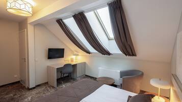 A bedroom with a bed, a desk, a chair, a TV, and a skylight.