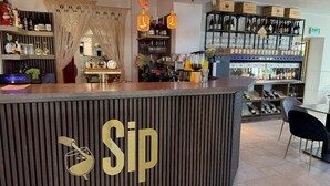 Zona de bar con una barra identificada con 'Sip', estantes con botellas y una cava de vinos.
