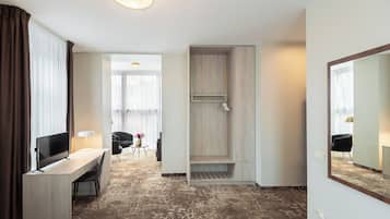 Habitación de hotel con escritorio, silla, televisor, ducha y un espejo grande.