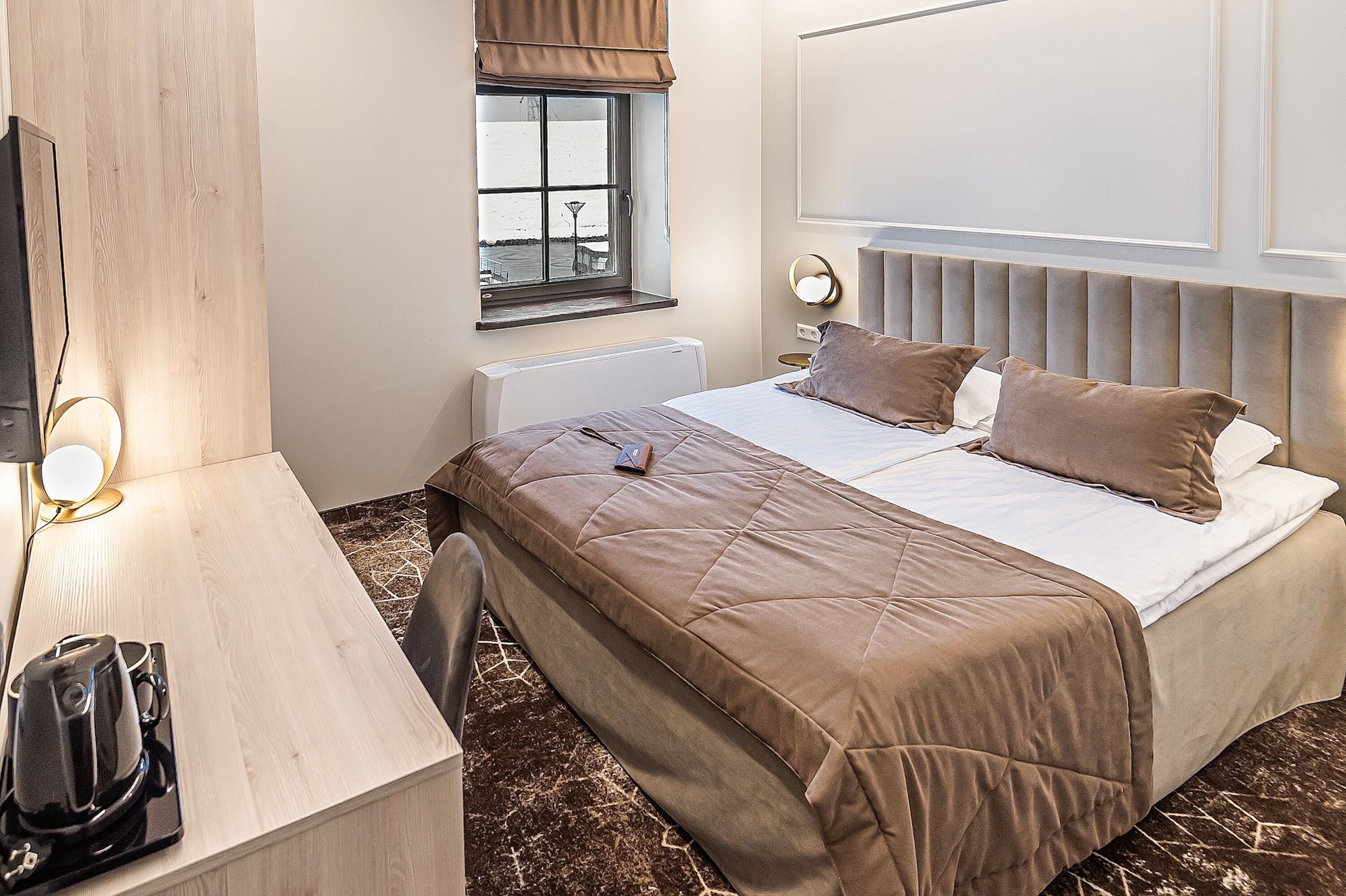 A hotel room with a bed, bedside table, lamp, and a window with a view.