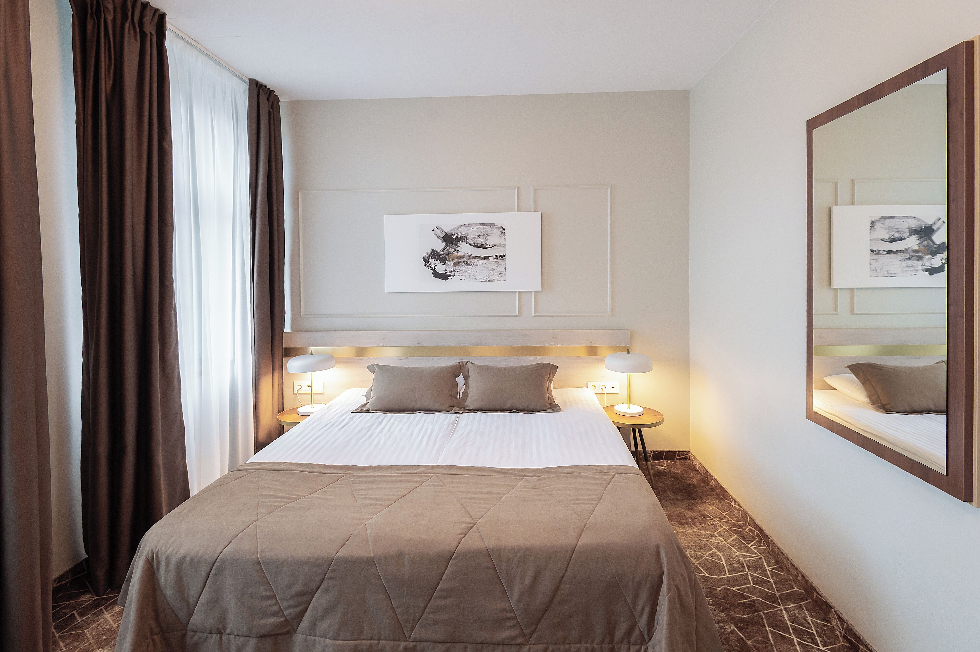 Habitación de hotel con una cama grande, una lámpara de noche, una obra de arte en la pared y un espejo.