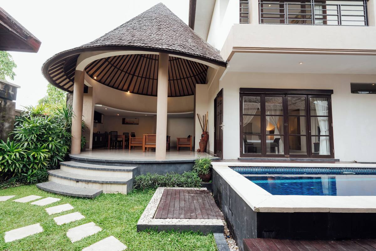 Ein modernes Haus mit überdachter Terrasse, Swimmingpool und gepflegtem Garten.
