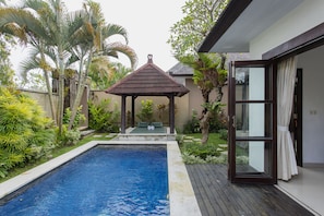 Relax by the serene pool surrounded by lush vegetation and a shaded gazebo.