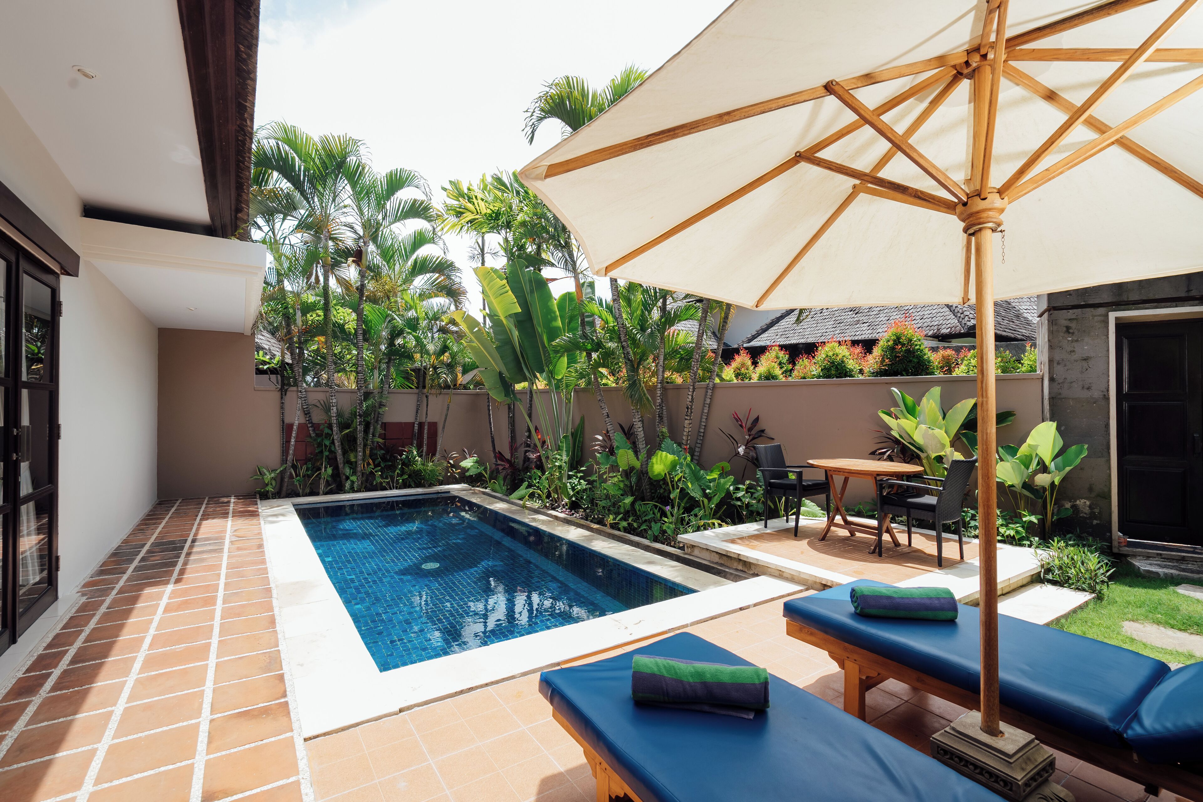 Piscina com espreguiçadeiras e guarda-sol, rodeada por plantas tropicais.