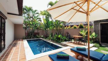 Piscina com espreguiçadeiras e guarda-sol, rodeada por plantas tropicais.