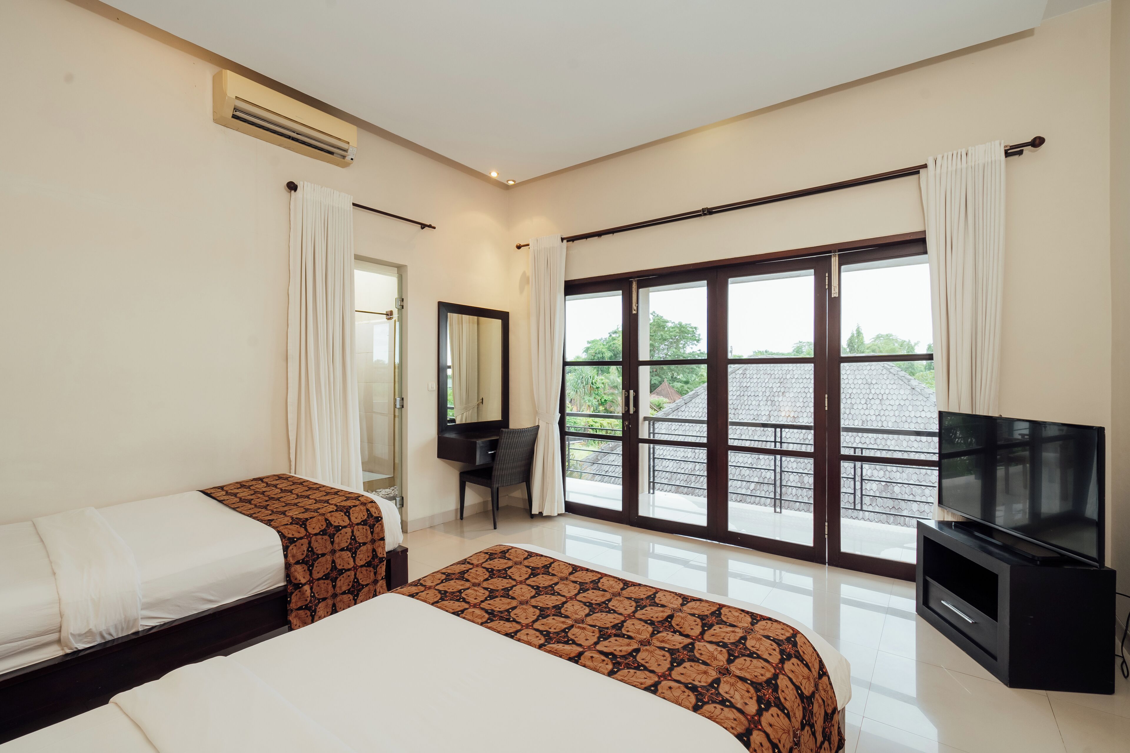 A hotel room with two beds, a desk, a TV, and a balcony with a view.