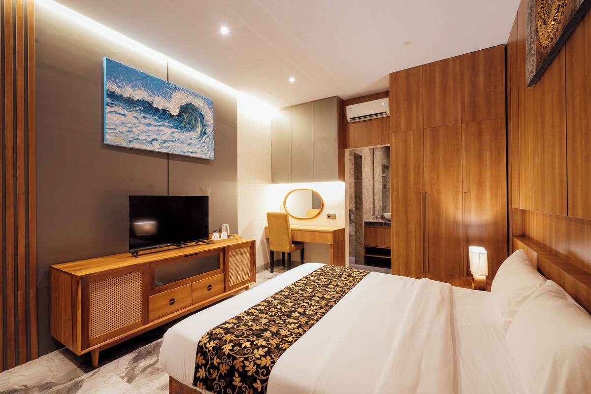 Ein Hotelzimmer mit einem Bett, einem Holztisch, einem Fernseher, einem Spiegel und einem Bild an der Wand.