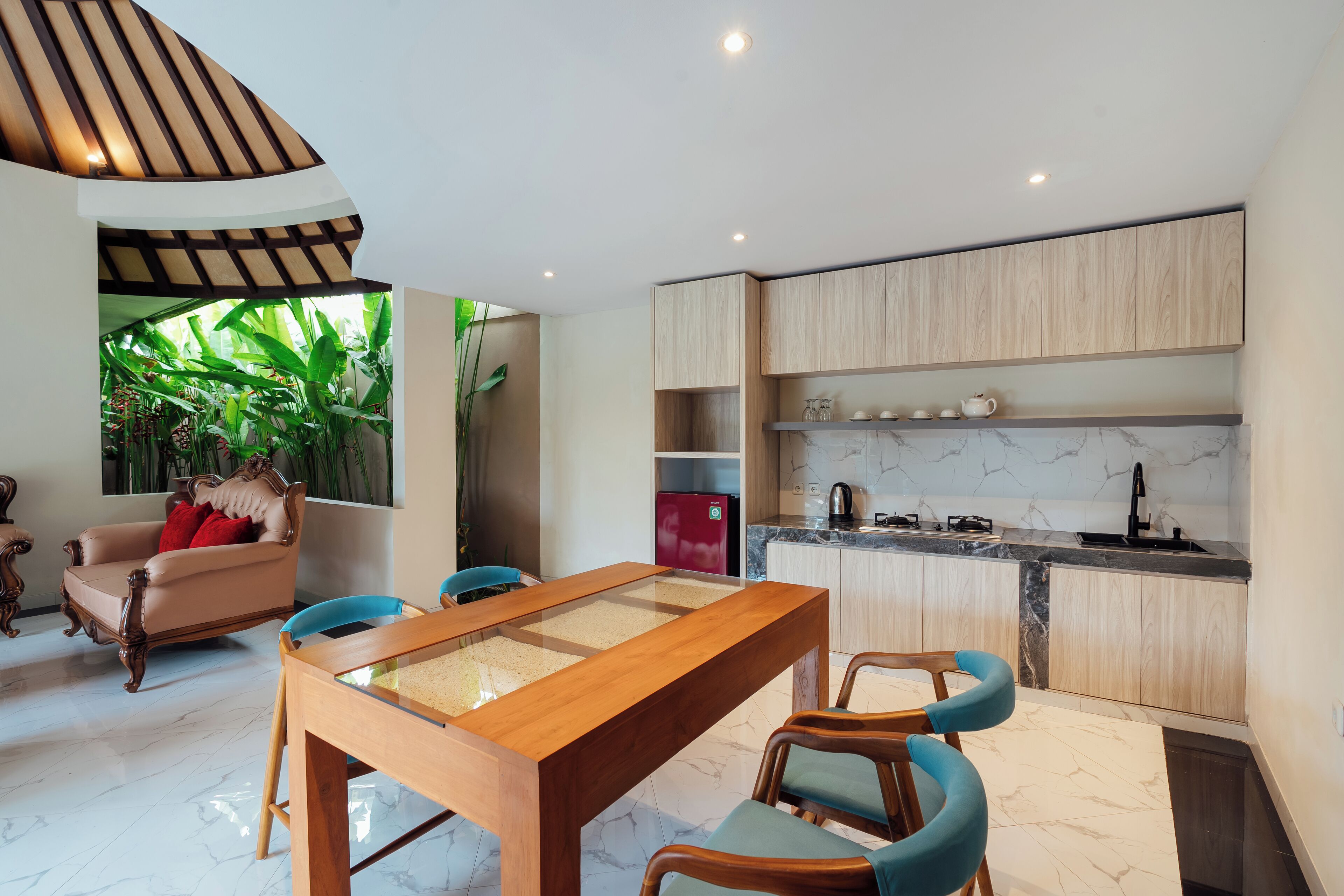A modern kitchen with wooden cabinets, a marble countertop, and a dining area with a glass-top table and wooden chairs.