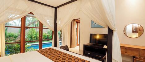 A bedroom with a large bed, a TV, a desk, and a view of a swimming pool.