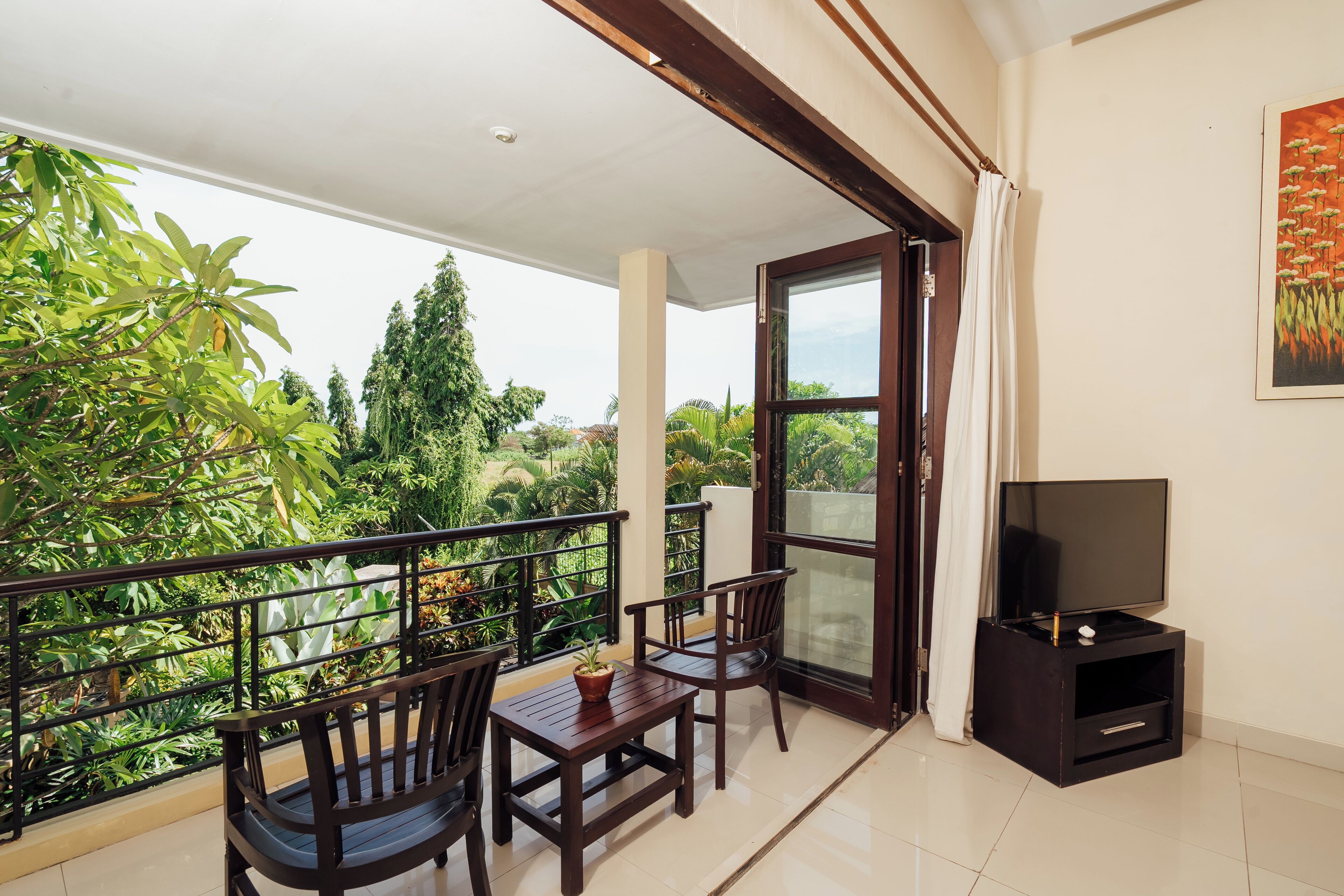 A balcony with a TV stand, two chairs, a small table, and a potted plant.