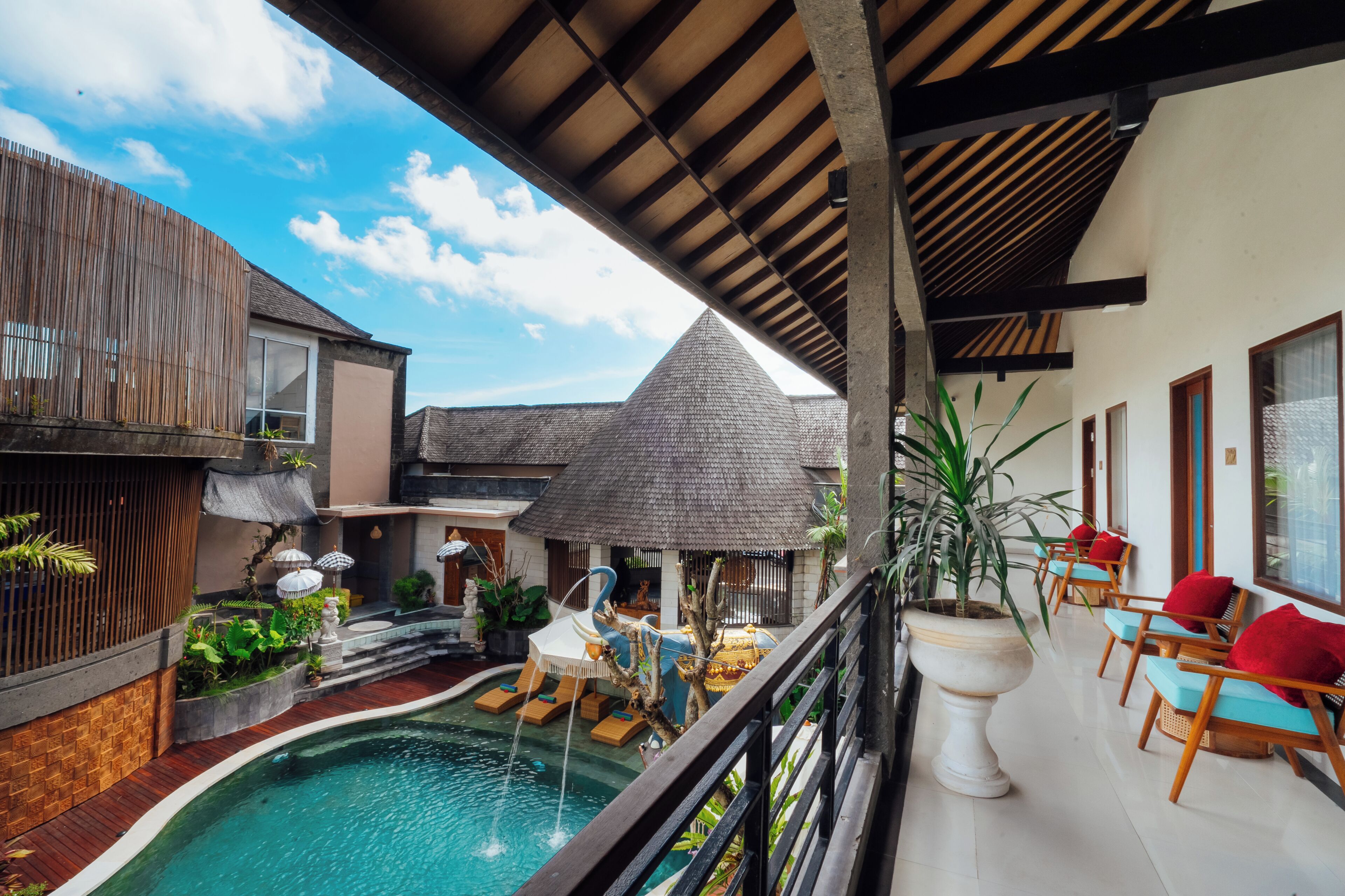 A pool area with a wooden deck, lounge chairs, and a thatched-roof structure.