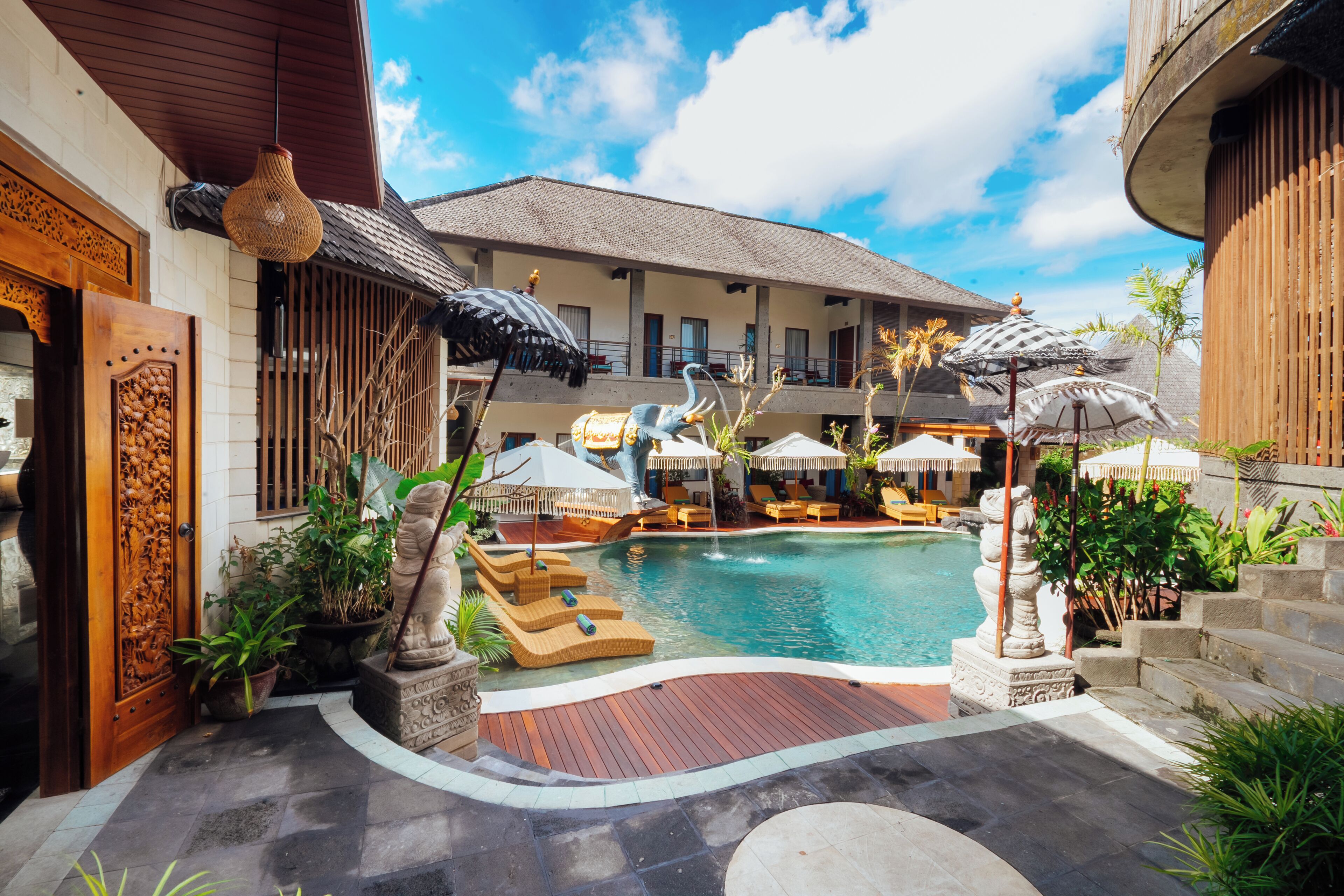 A pool area with lounge chairs, umbrellas, and a stone statue.