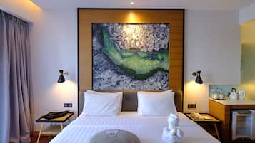 Una camera d'albergo con un letto grande, due abat-jour, un quadro appeso al muro, una piccola scrivania con un bollitore e un minibar.