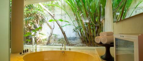 A bathroom with a large bathtub, a sink, and a mirror. There are towels on a stand and a television on the right side.