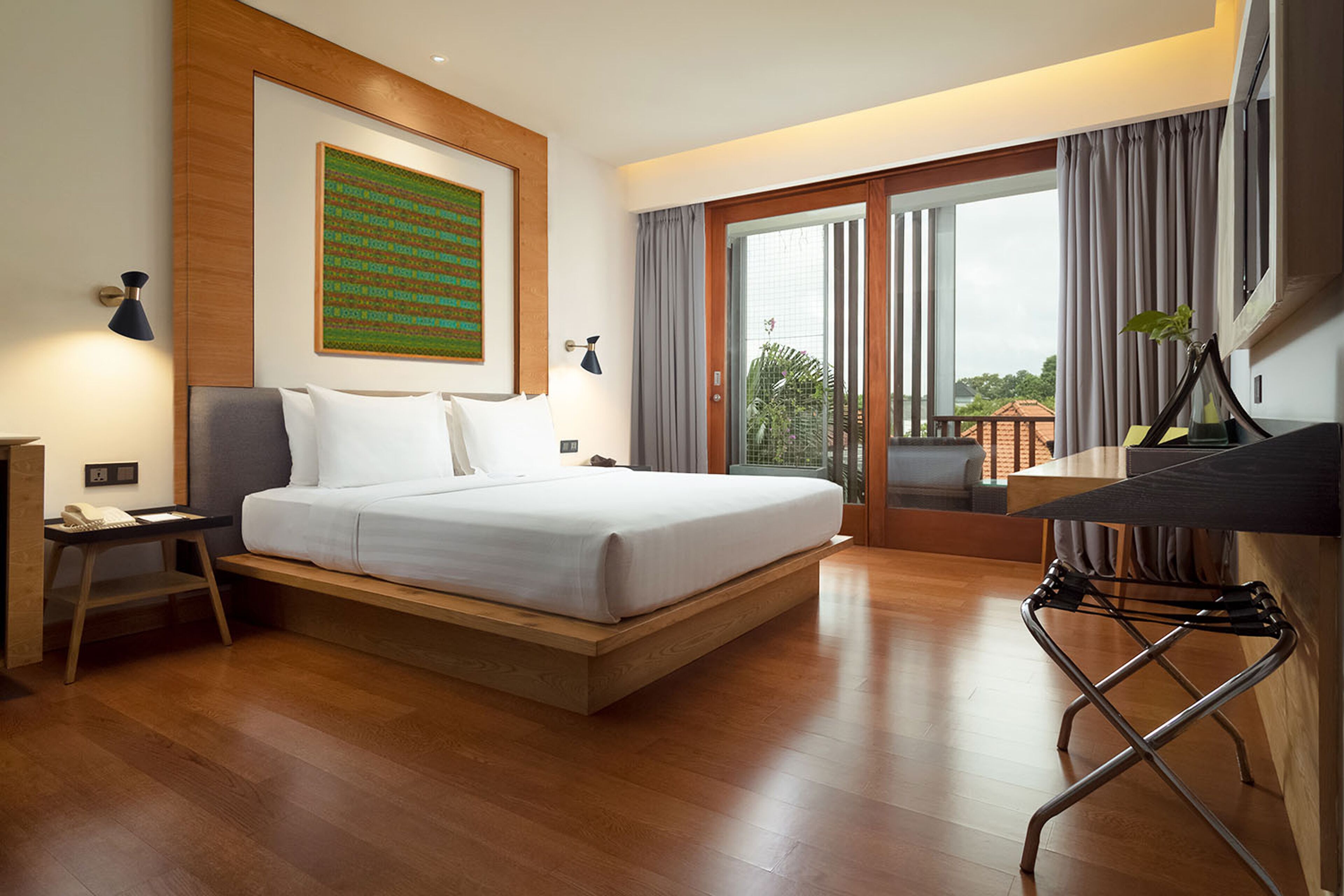 A modern hotel room with a large bed, a desk, and a view of the outdoors.