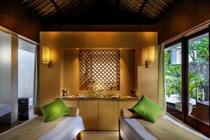 A room with two beds, a wooden partition, and a view of greenery outside.