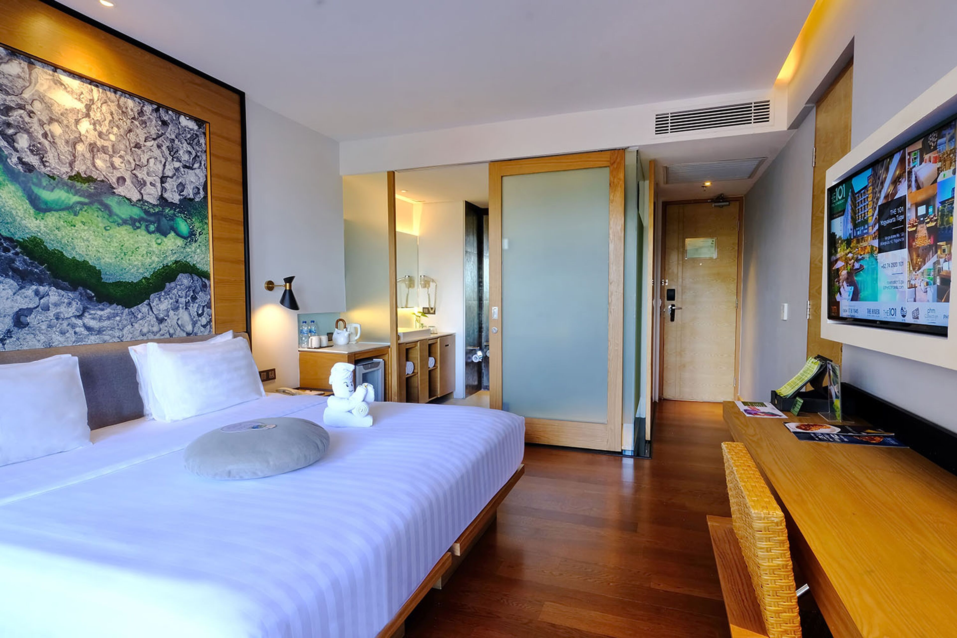 Una camera d'albergo con un letto grande, una panca di legno, una TV e un quadro appeso al muro.