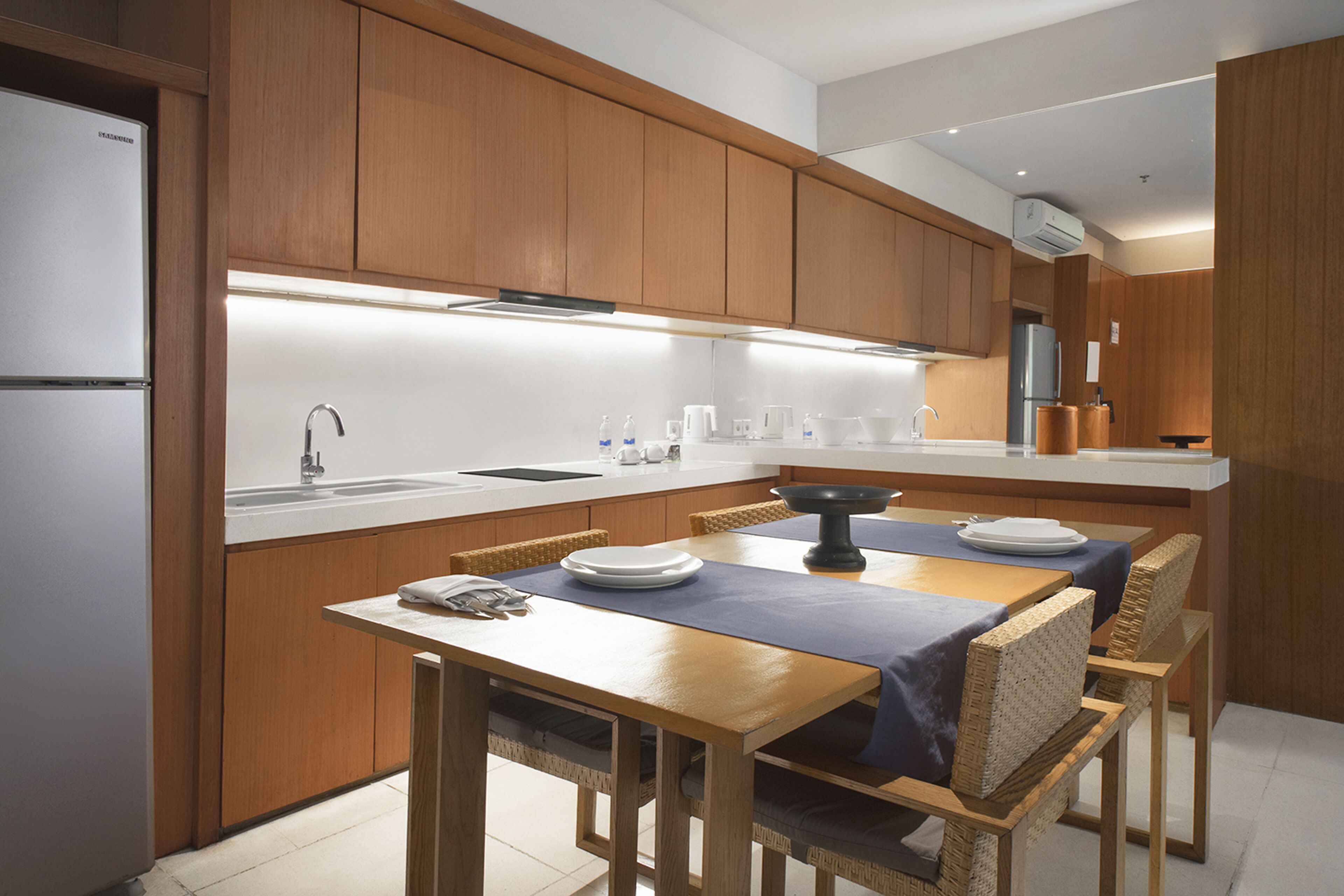 A modern kitchen with wooden cabinets, a stainless steel refrigerator, a sink, and a dining area with a table and chairs.