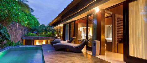 A modern outdoor pool area with lounge chairs, a wooden deck, and a well-lit interior space.