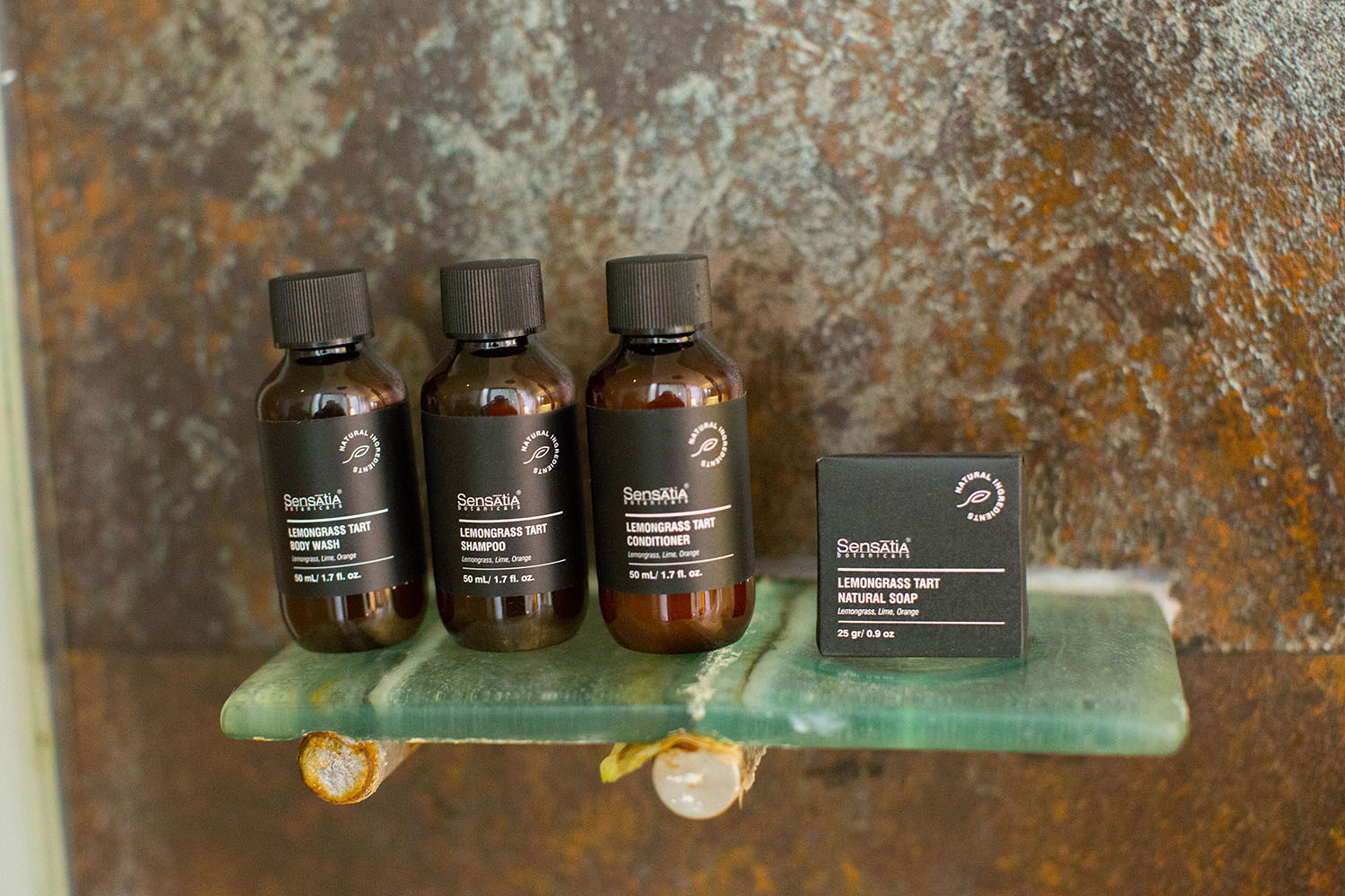 Três frascos de Sensatia líquido de banho e uma caixa de sabonete natural Sensatia sobre uma prateleira verde em frente a uma parede texturizada.