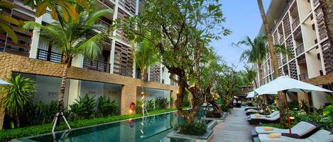 A poolside area with lounge chairs and umbrellas, surrounded by palm trees and greenery.