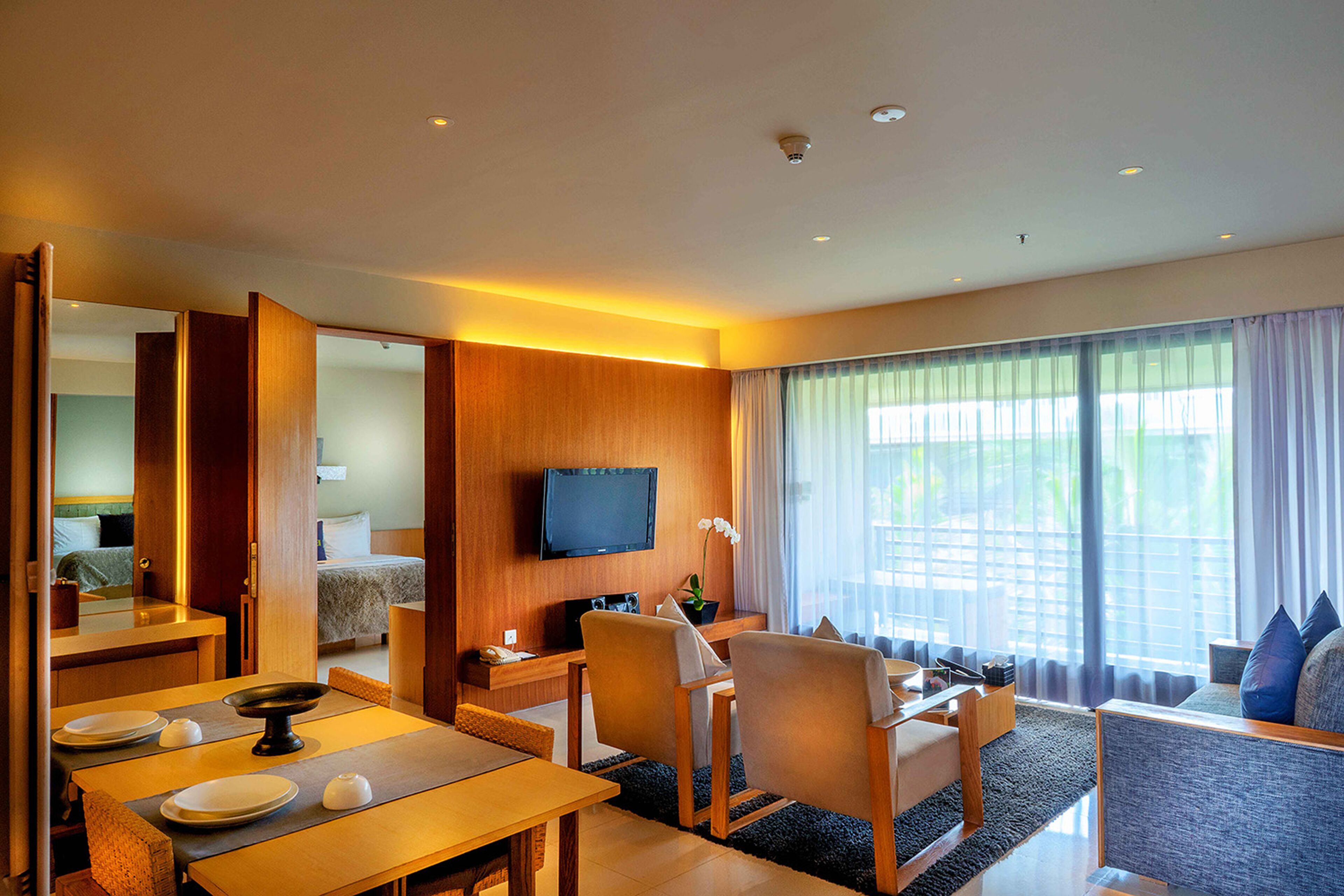 Une chambre d’hôtel comprenant un coin repas, un téléviseur fixé au mur, un lit donnant sur l’extérieur et une grande fenêtre avec des rideaux.
