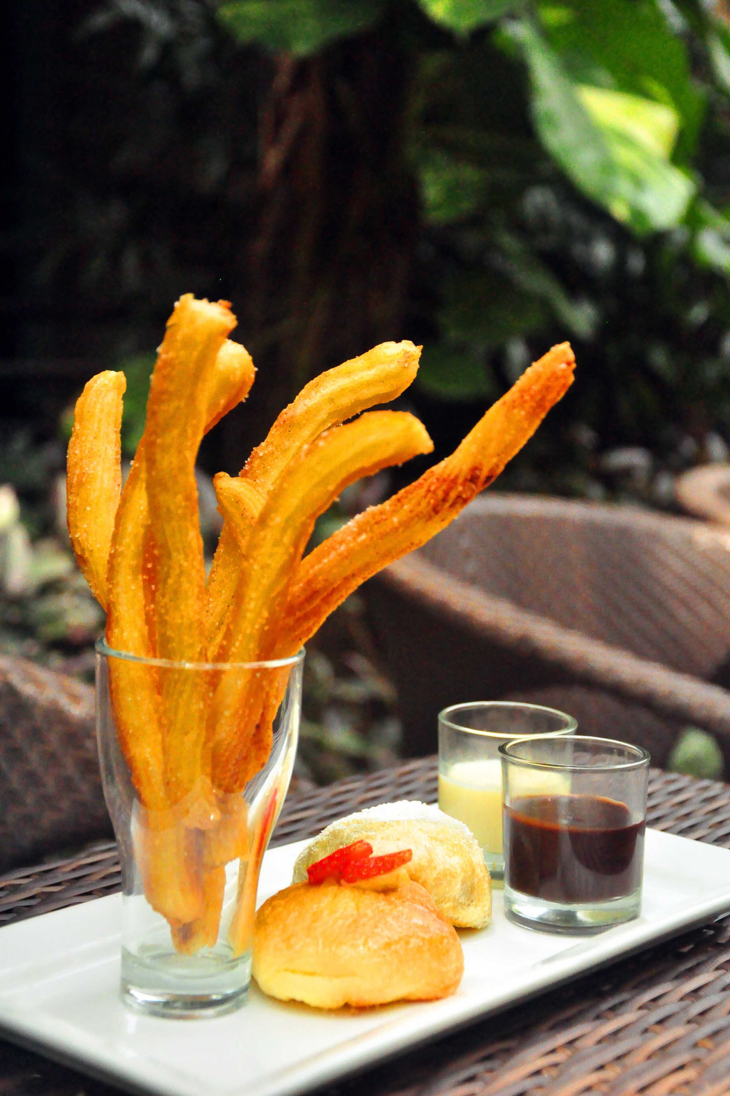 Un plato con churros, un vaso de leche y un vaso pequeño de salsa de chocolate.