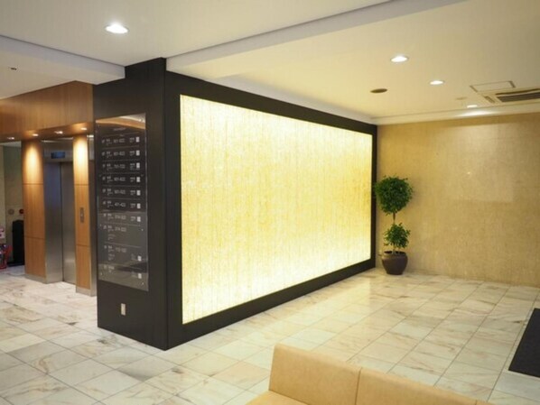 Un vestíbulo moderno con una gran pared iluminada, un mostrador de recepción y una planta en maceta.