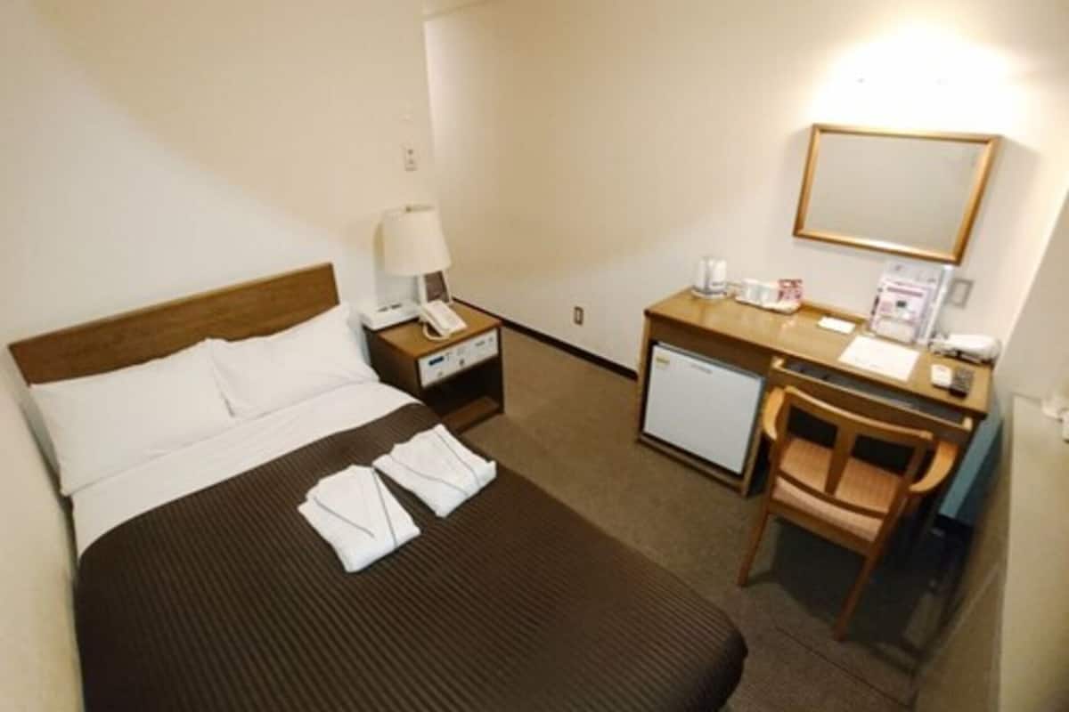 A hotel room with a bed, a desk, a chair, a small desk lamp, a telephone, and a mirror.