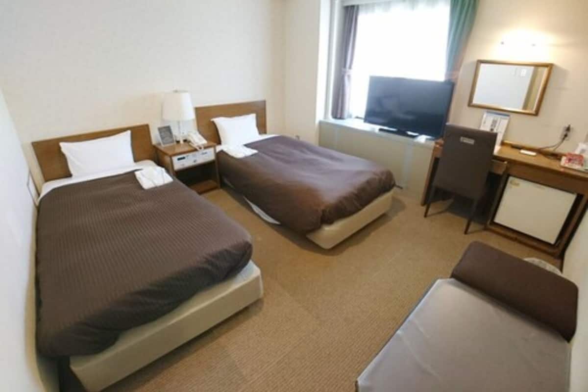 A hotel room with two beds, a desk, a chair, a TV, and a window with curtains.