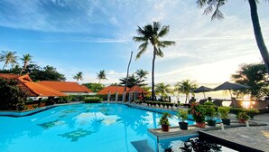 Une piscine dont le fond est recouvert de carrelage, entourée de palmiers et surplombée d’un ciel dégagé.