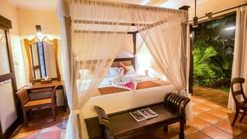 Habitación de hotel con cama con dosel, una mesita, una silla, un espejo y vista a un jardín.