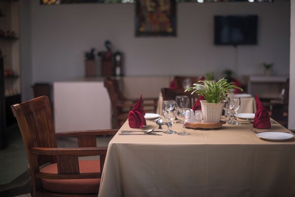 A dining table set with plates, glasses, and a potted plant, surrounded by wooden chairs. - Nugraha Lovina Seaview Resort & Spa (Banjar)