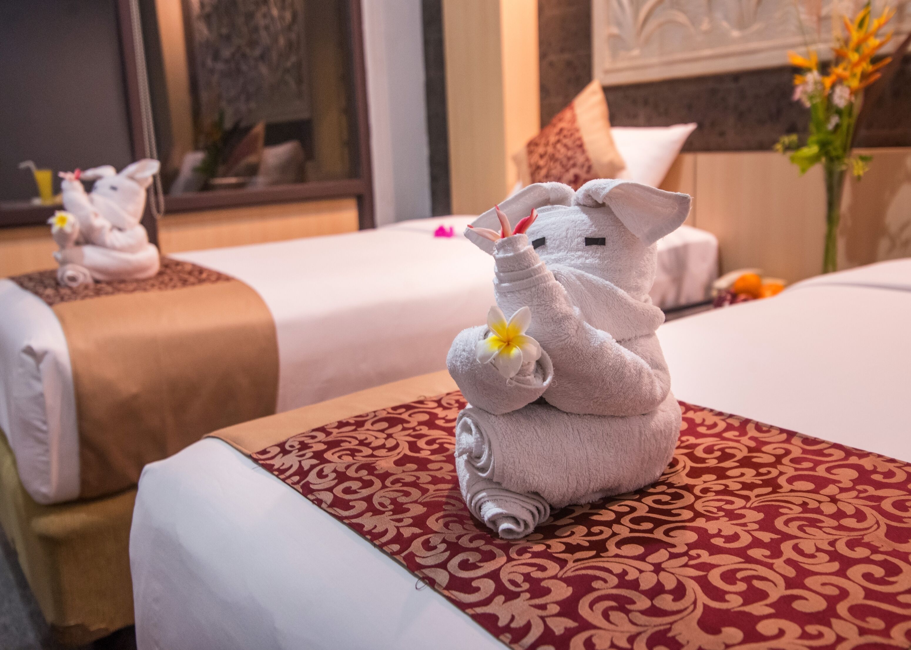 A hotel room with two beds, each with a towel animal sculpture and a flower.